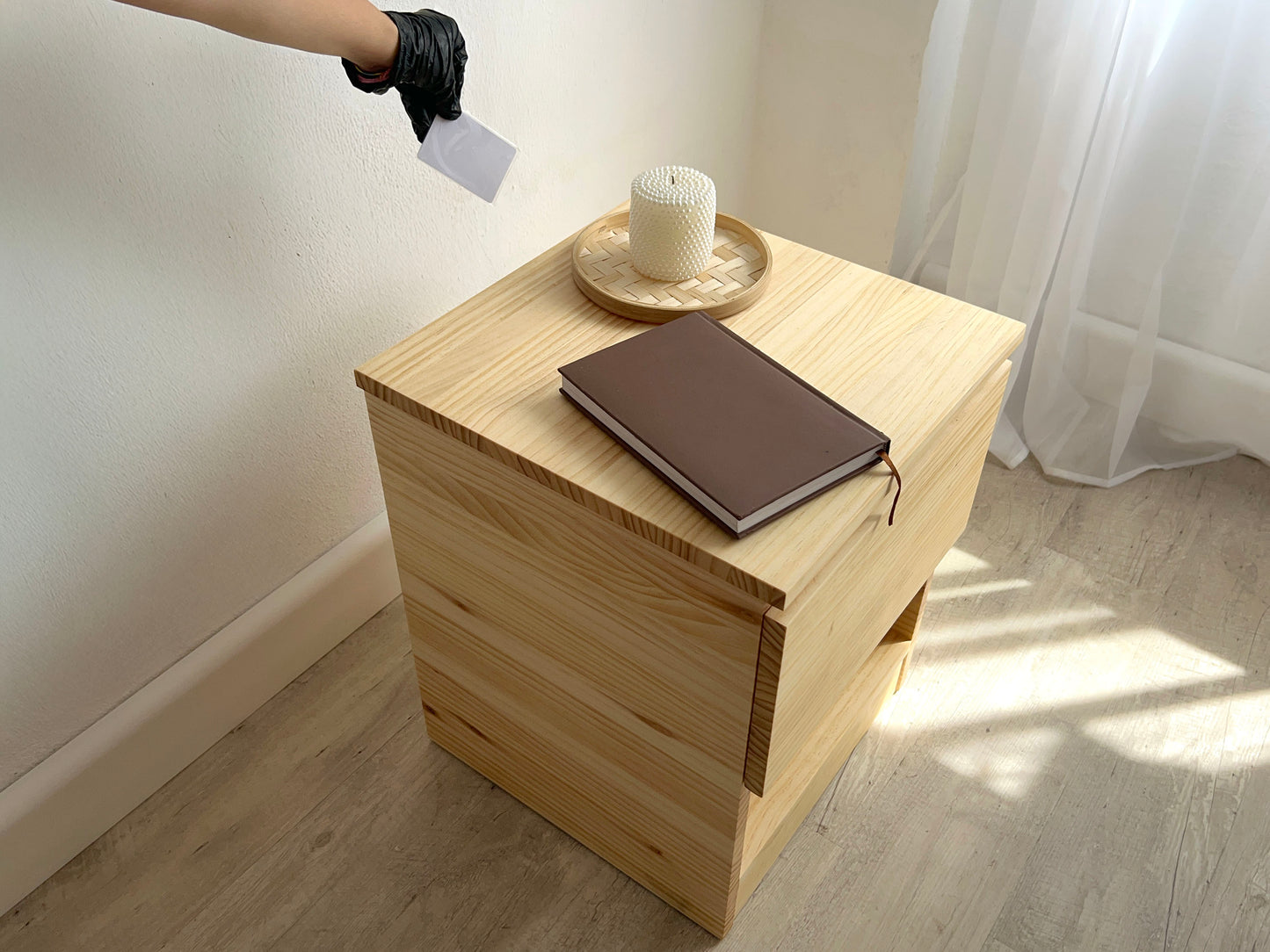 Mesita de pino macizo Beetle Wood con compartimento secreto integrado y apariencia convencional en ambiente de habitacion con decoracion y acercando en una mano una tarjeta rfid para su apertura