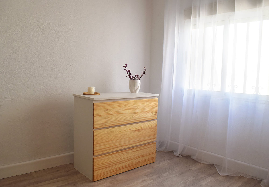 Cassettiera Beetle Wood bianca con frontali in pino accanto a una finestra con tende chiare, un mobile discreto per il soggiorno