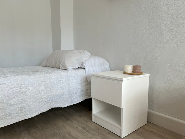 Wit Beetle Wood® nachtkastje met lade naast een bed in een lichte slaapkamer