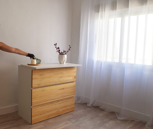 Vista lateral de comoda grande blanca con frontales en pino macizo con espacio oculto Beetle Wood de líneas limpias y diseño sobrio introduciendo en interior dinero en efectivo
