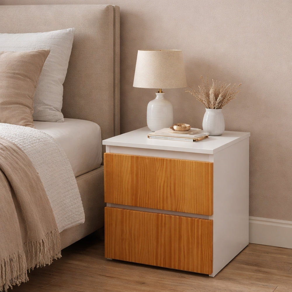 Mesita de noche moderna blanca con cajones y acabado en madera junto a cama